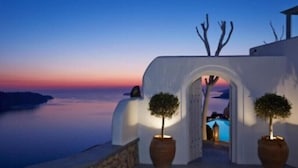 An arched entrance with potted trees, leading to a pool area with a view of the sea at sunset. - Athermi Suites - Adults Only (Santorini)