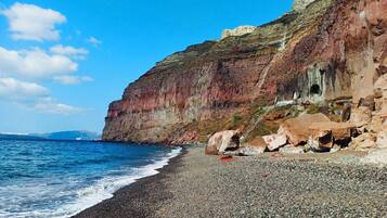 Une plage de galets, avec une falaise rocheuse et un ciel bleu dégagé.