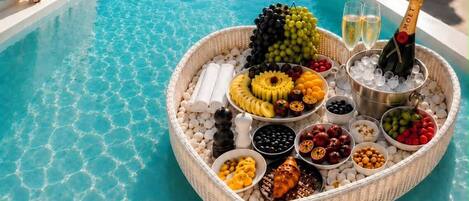 A poolside buffet with a variety of fruits, cheeses, and a bottle of champagne.