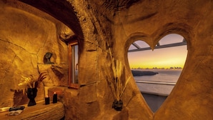 A room with a heart-shaped window, a wooden shelf with candles, and a vase with feathers. - Athermi Suites - Adults Only (Santorini)