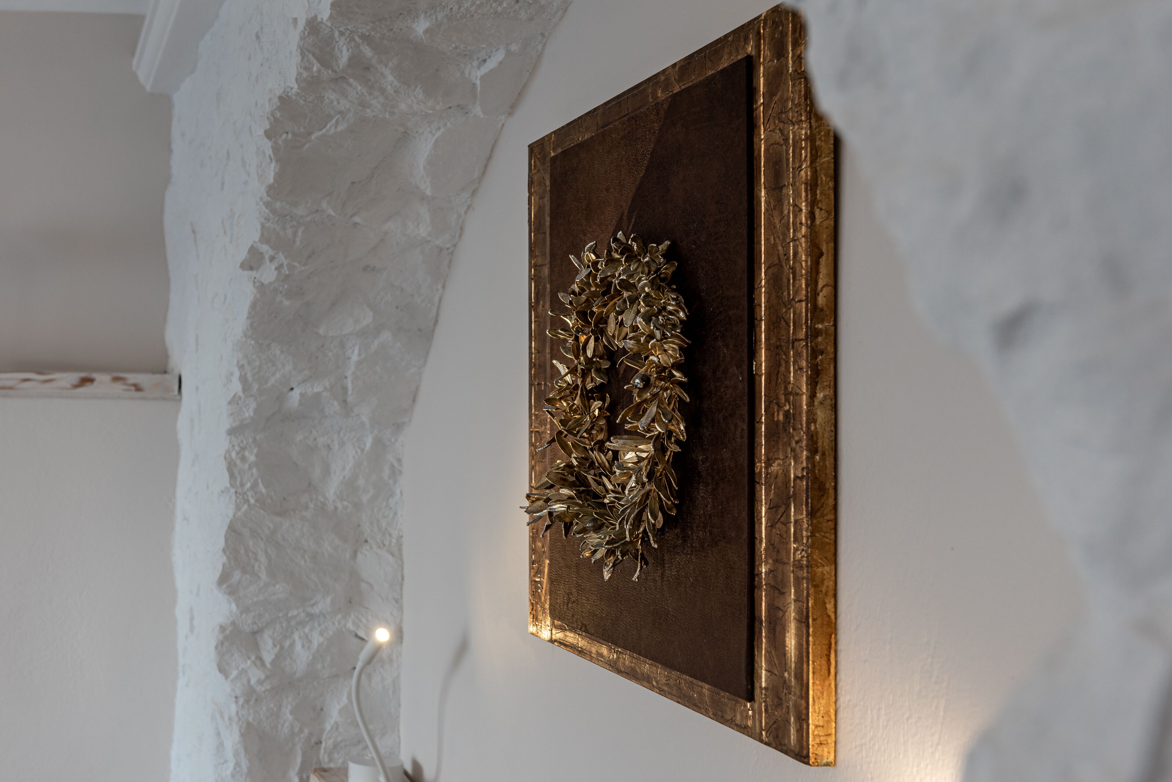 A wall with a textured white surface and a framed artwork with a golden wreath.