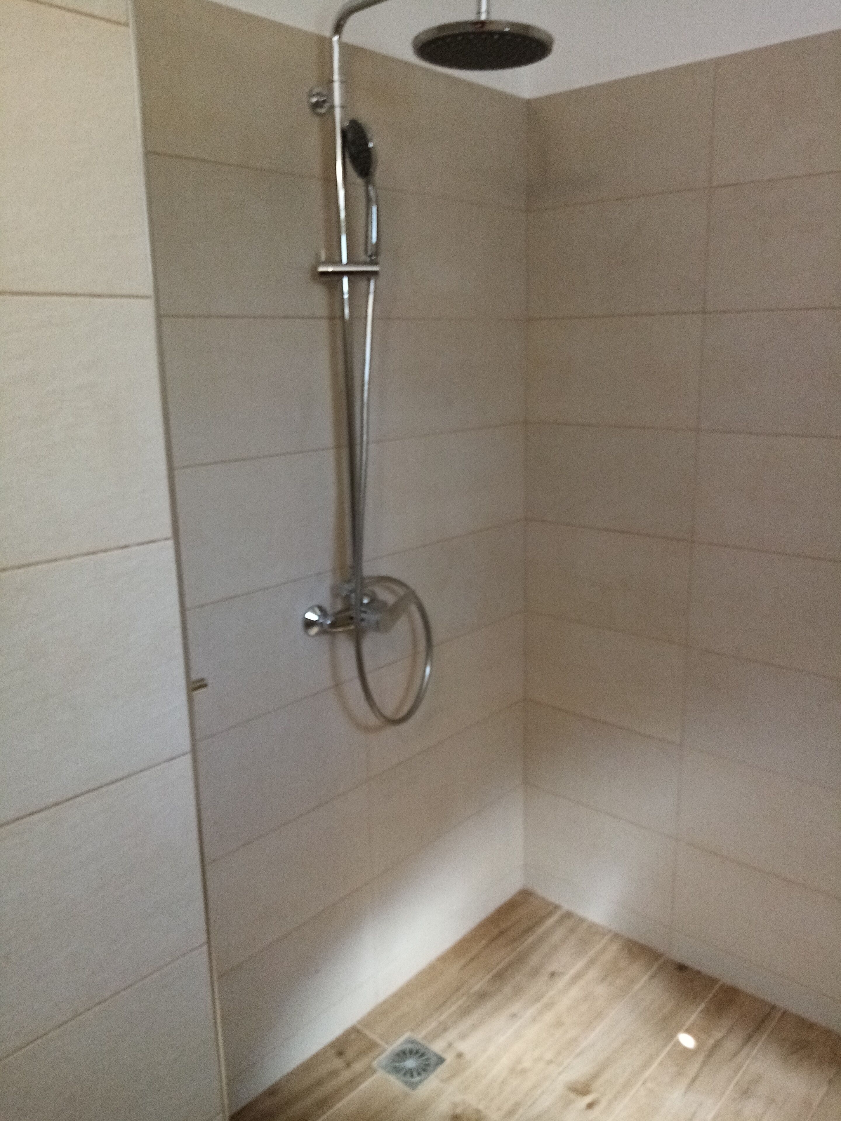 A shower area with a handheld showerhead, a wall-mounted faucet, and a floor drain.