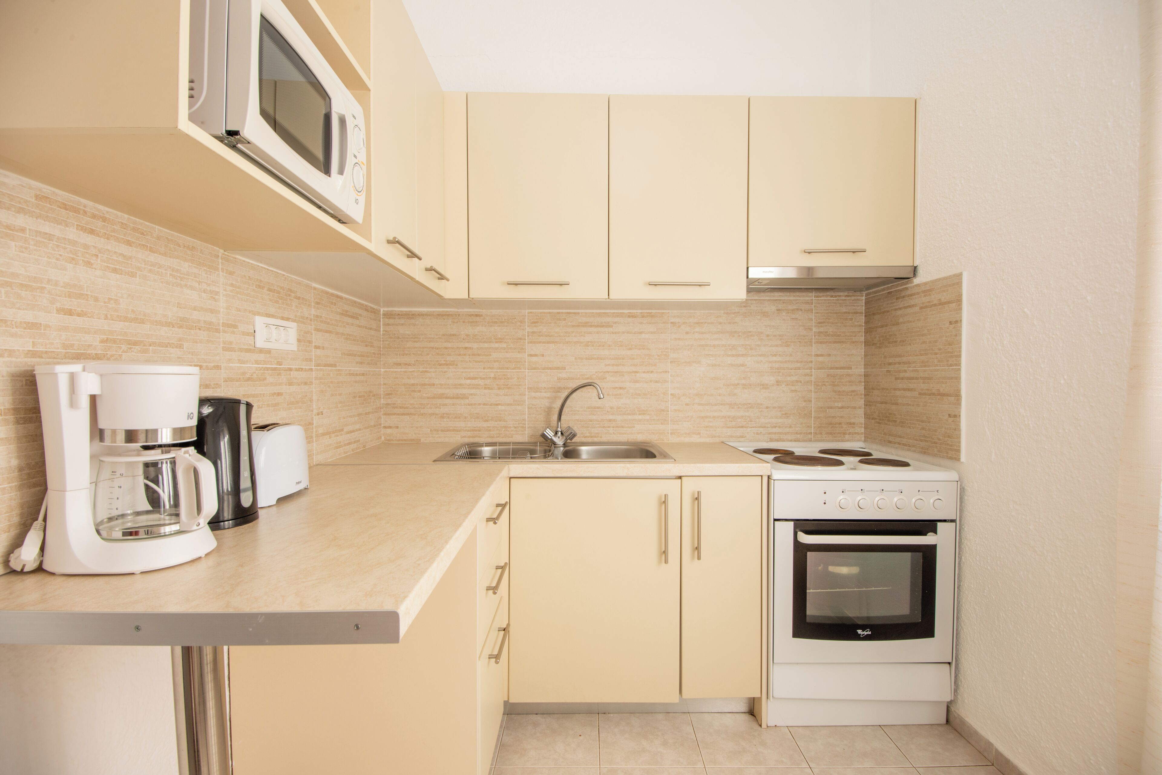 A kitchen with a microwave, coffee maker, toaster, sink, and stove.