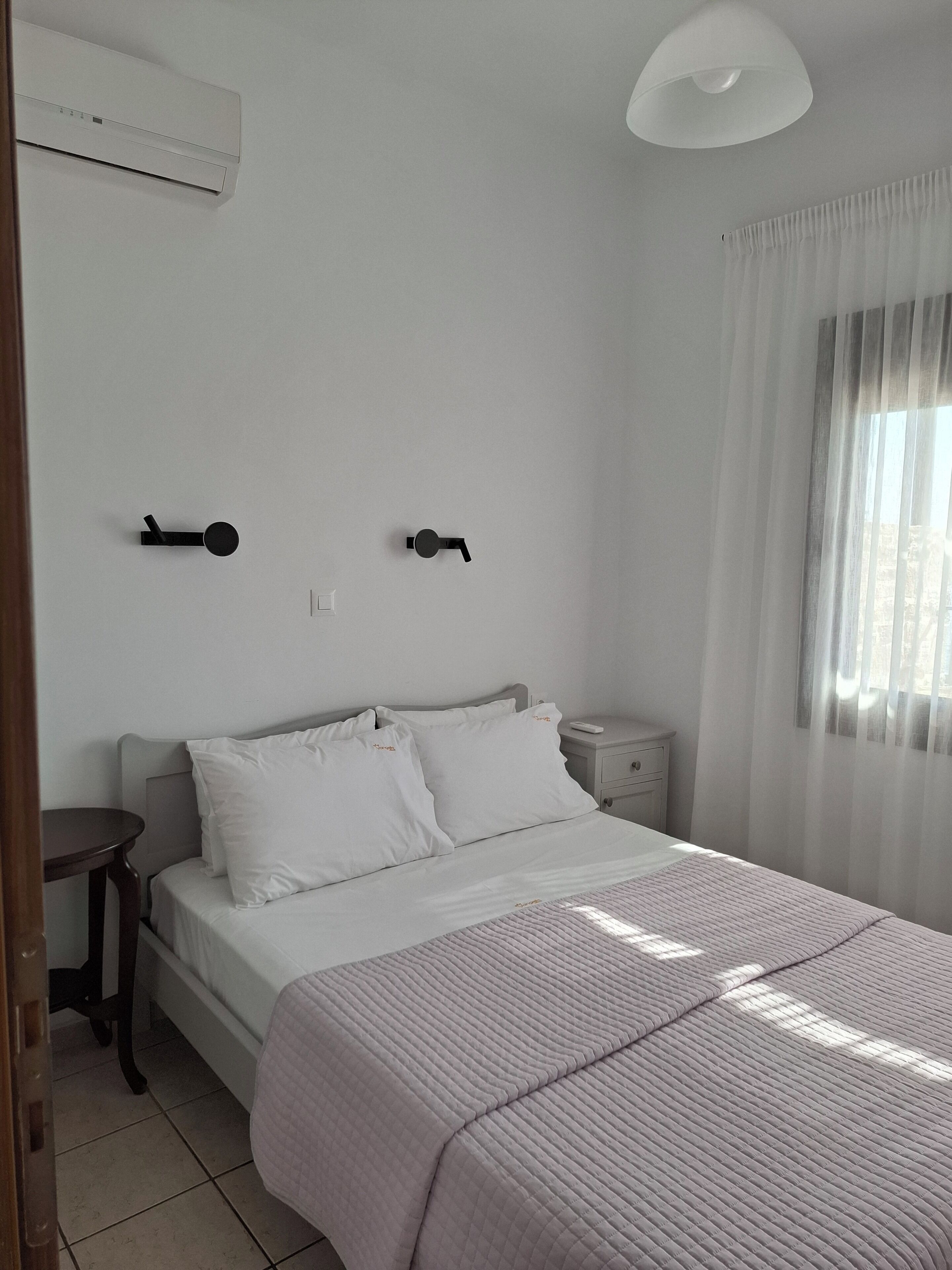 A bedroom with a bed, bedside tables, a nightstand, an air conditioning unit, and a window with curtains.