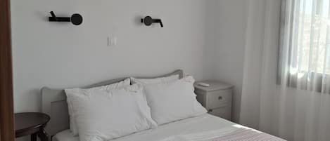 A bedroom with a bed, bedside tables, a nightstand, an air conditioning unit, and a window with curtains.