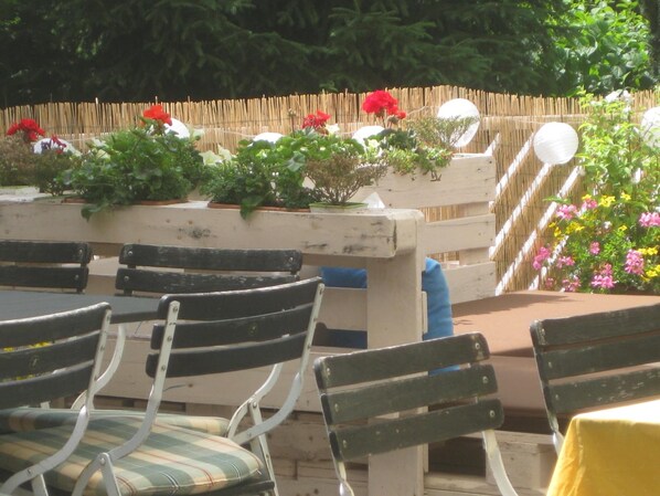 Een terras met houten banken en stoelen, omgeven door potplanten en bloemen.