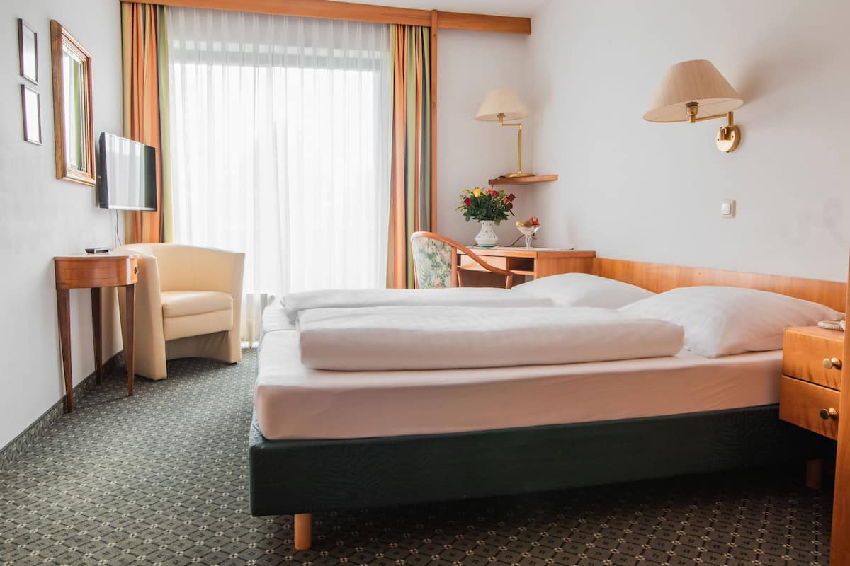 Een hotelkamer met een bed, een bureau, een stoel, een televisie en een raam met gordijnen.