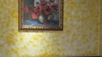A dining area with a table set for two, a vase with flowers, and a framed painting on the wall.
