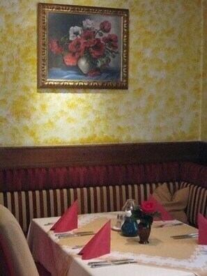 Een eetgedeelte met een tafel gedekt voor twee personen, een vaas met bloemen en een lijst met een schilderij aan de muur.