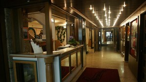 Een hotelgang met een receptiebalie, houten lambrisering en een rood tapijt.