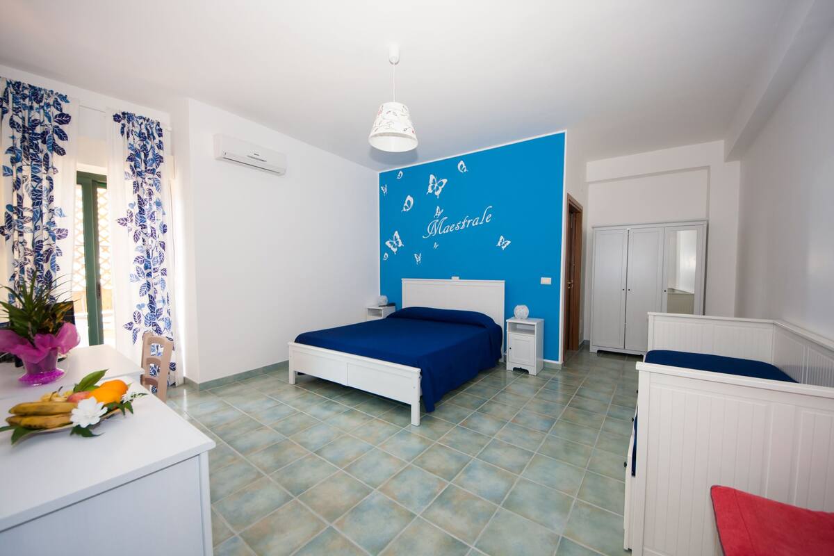Ein Schlafzimmer mit Bett, Nachttisch, Kommode und einem Fenster mit Vorhängen.