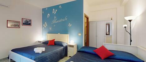 A hotel room with two beds, a blue accent wall, a mirror, a wardrobe, and a bedside table with a lamp.
