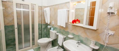 Un baño con ducha, inodoro, bidé, lavabo y un secador de pelo en la pared.