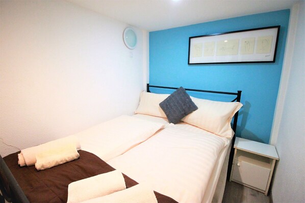 A neatly made bed with a blue wall and a framed picture above it.
