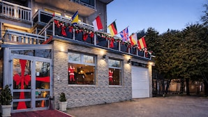 A modern building with a stone facade, large windows, and a red carpet entrance. Flags are displayed on the balcony. - Hotel Villa Harmony (Sarajevo)