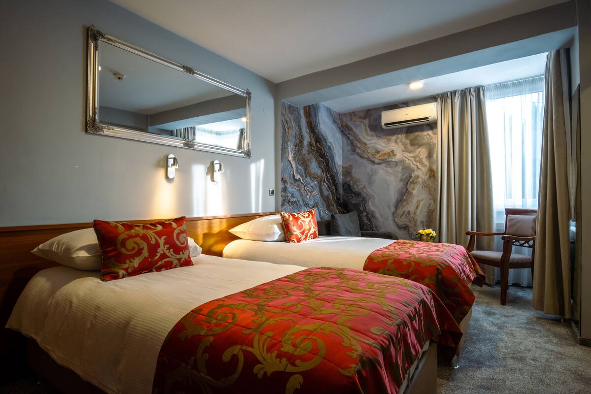 Ein Hotelzimmer mit zwei Betten, einem großen Spiegel, einer Marmorwand, einer Klimaanlage und einem Sessel.