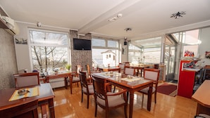 A dining area with wooden tables and chairs, a television mounted on the wall, and large windows offering a view of the outside. - Hotel Villa Harmony (Sarajevo)