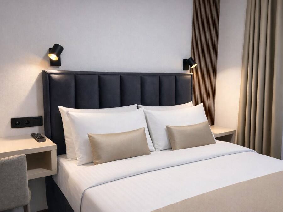 Una habitación de hotel moderna con una cama grande, dos mesitas de noche, un control remoto y luces de lectura fijadas en la pared.