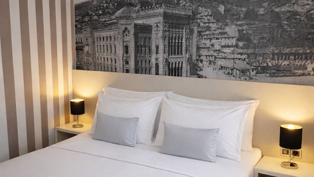 A hotel room with a bed, two bedside tables, and a large wall-mounted picture. - Hotel Villa Harmony (Sarajevo)