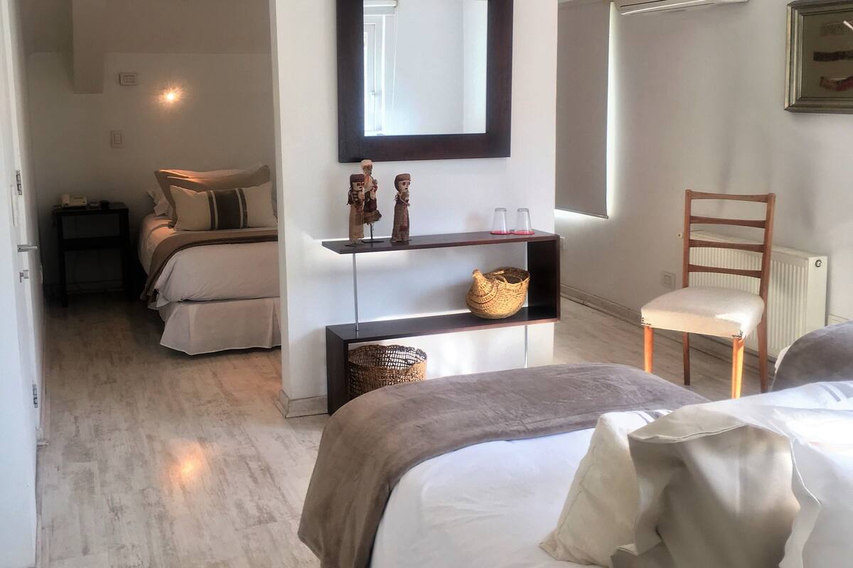 A bedroom with a large bed, a bedside table, a chair, a mirror, and a shelf with decorative items.