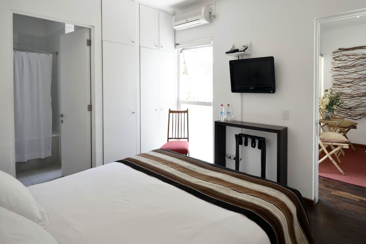 A hotel room with a bed, a TV mounted on the wall, a chair, and a small table with bottles.