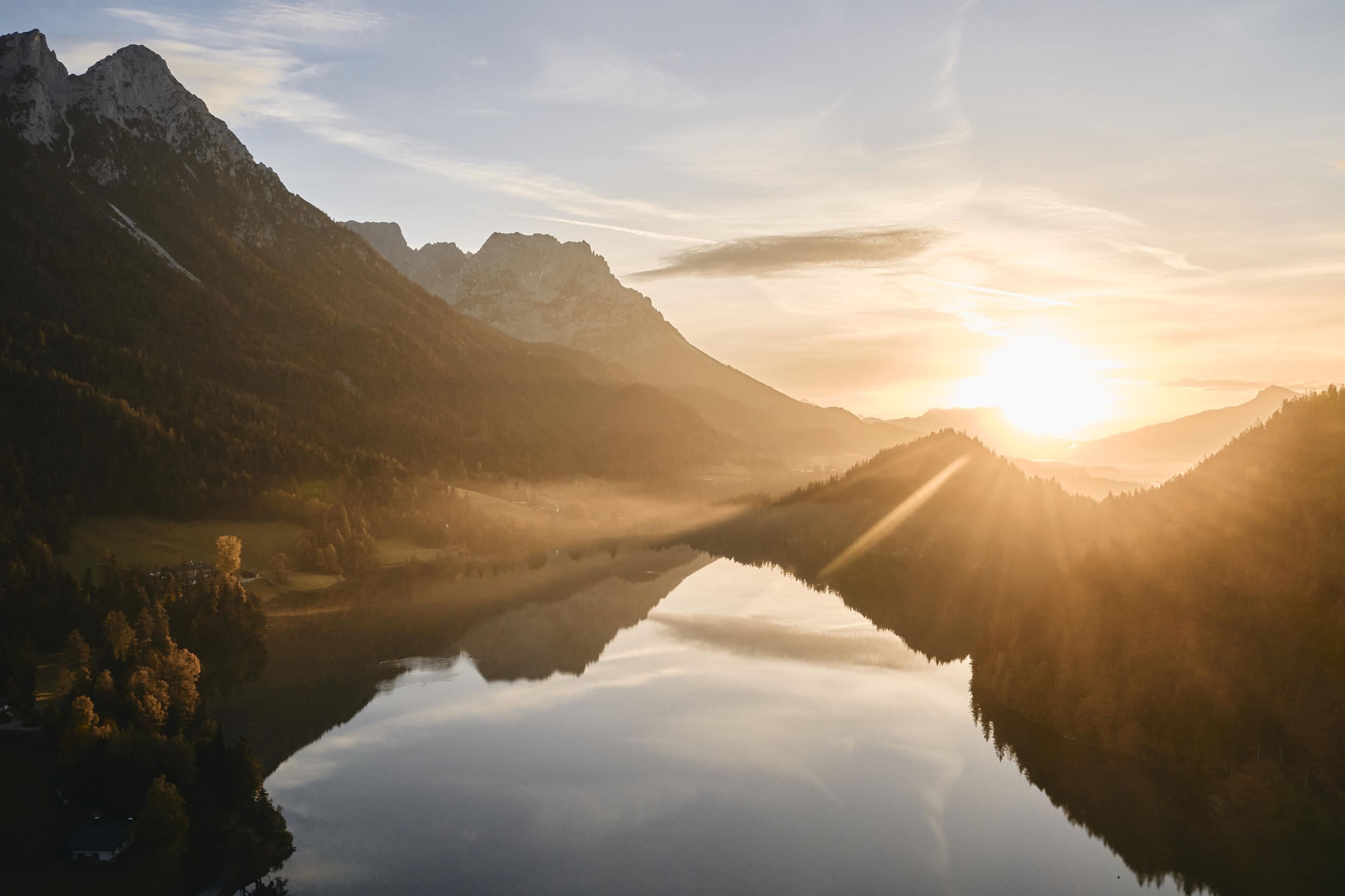Un lac de montagne paisible, illuminé par les premiers rayons du soleil, où se reflètent les sommets environnants et où le ciel est d’un bleu limpide.