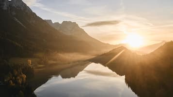 Un lac de montagne paisible, illuminé par les premiers rayons du soleil, où se reflètent les sommets environnants et où le ciel est d’un bleu limpide.