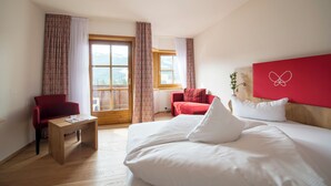 Ein Hotelzimmer mit einem Bett, zwei roten Sessel, einem Holztisch und einem großen Fenster mit Vorhängen.