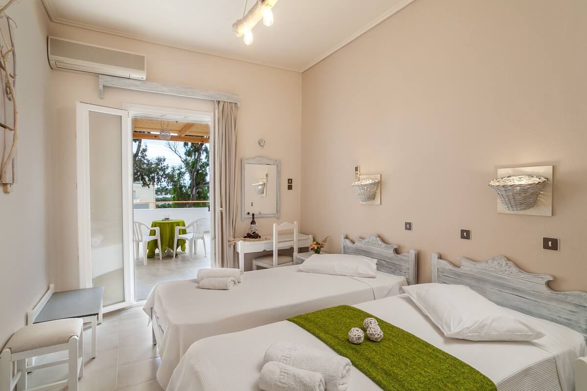 Habitación de hotel con dos camas, un escritorio y una silla. Tiene un balcón con mesa y sillas.