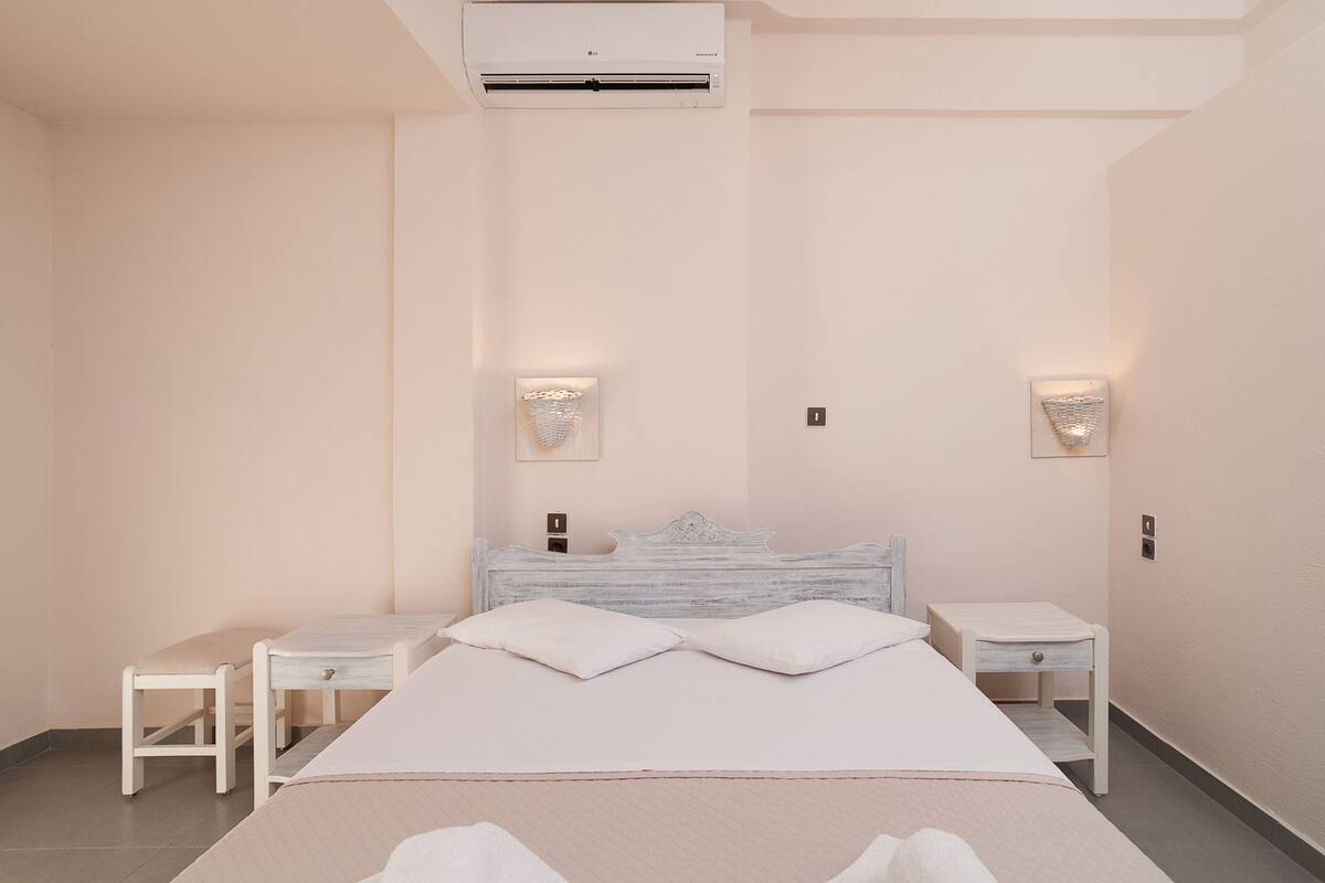 Un dormitorio con cama, dos mesitas de noche, un aire acondicionado de pared y dos apliques.