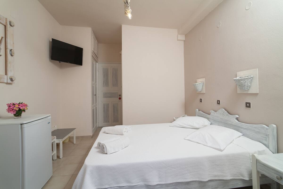 Un dormitorio ordenado con cama, mesitas de noche, televisor y un escritorio pequeño.