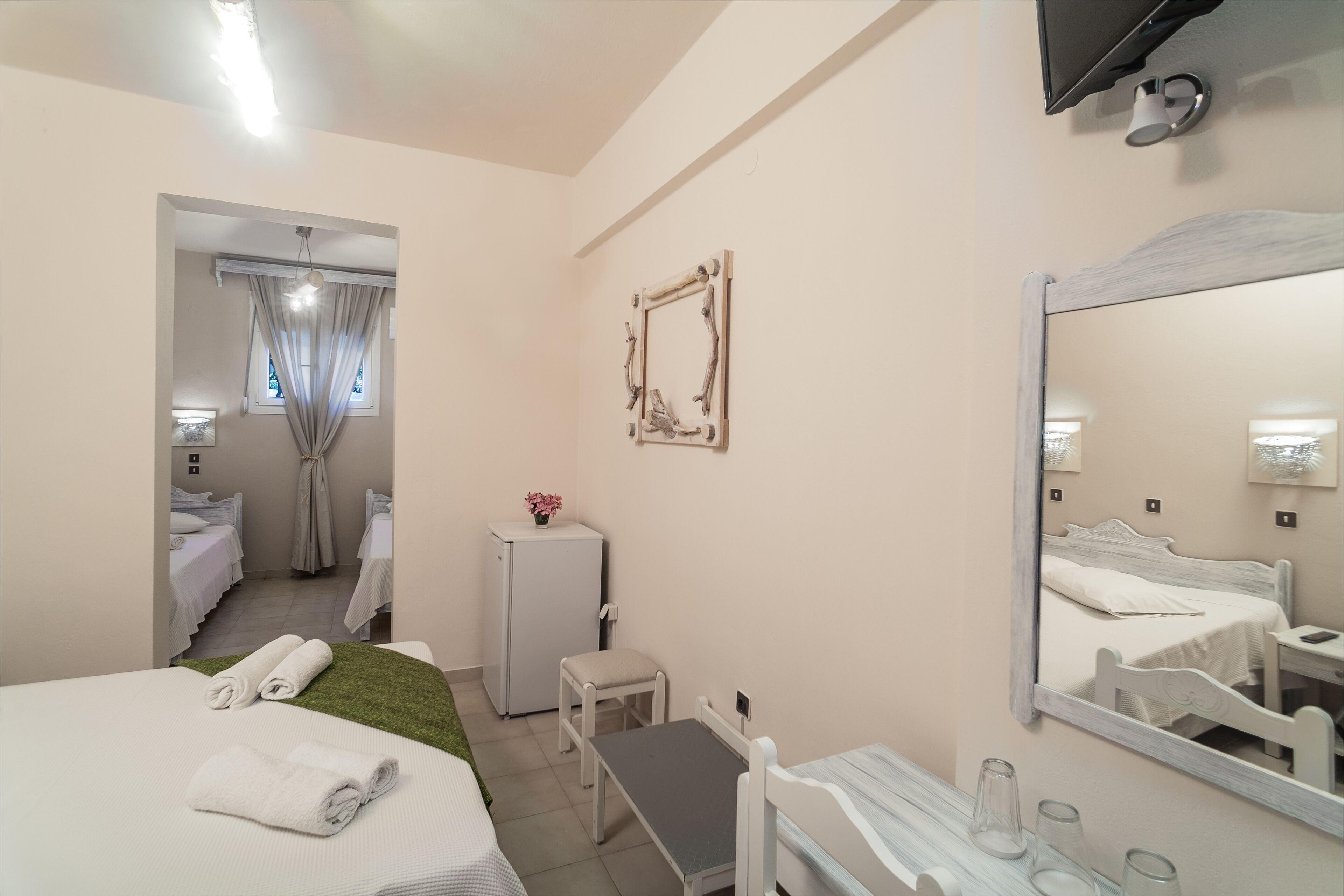 A hotel room with a bed, a desk, a chair, a small table, a refrigerator, a mirror, and a window with curtains.