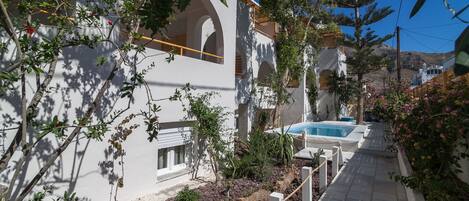A pool area with a stone pathway, white buildings with arches, and surrounding greenery.