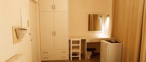 Habitación de hotel con cama, escritorio, armario y un refrigerador pequeño.