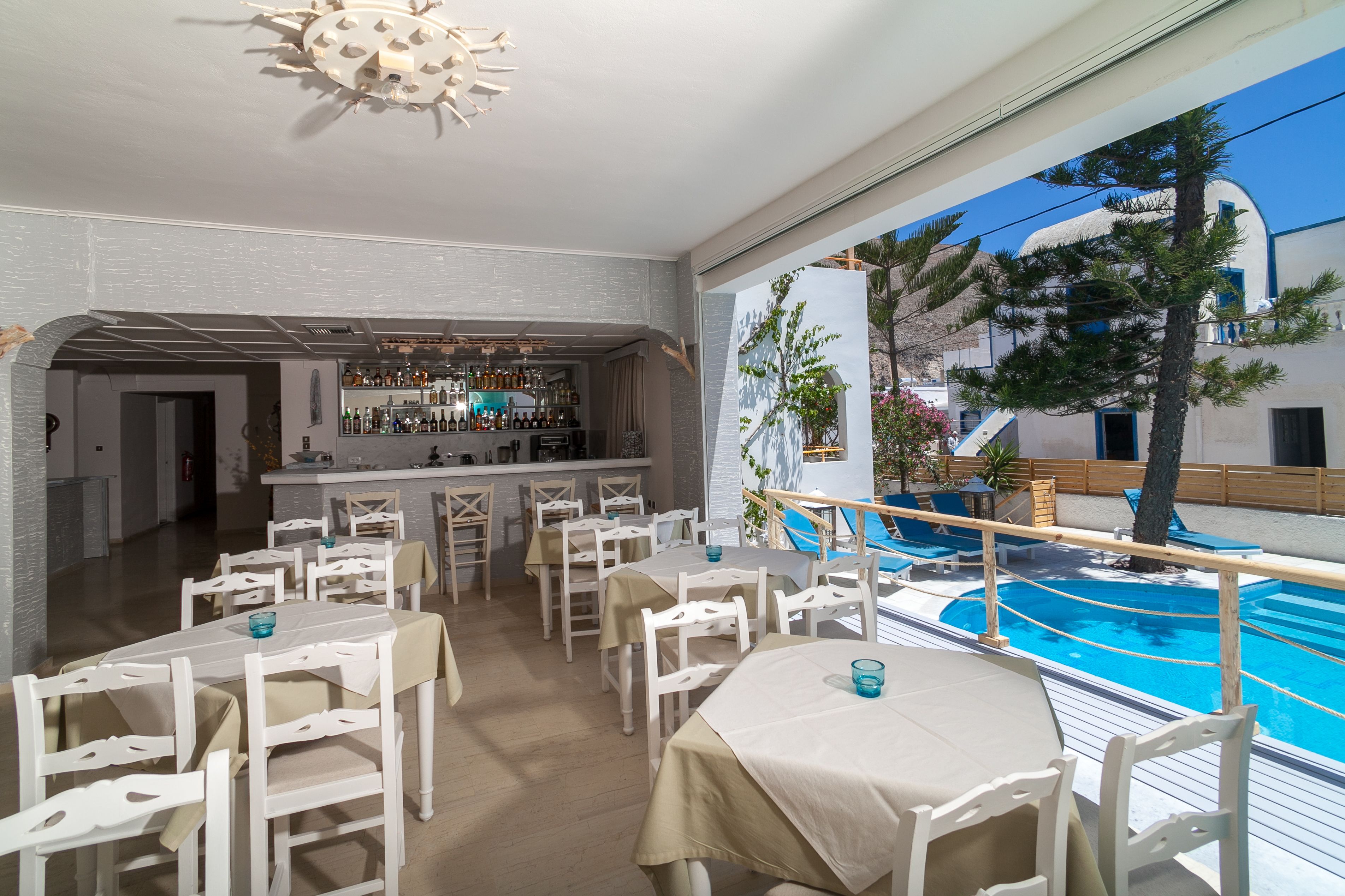 A bar area with a pool view, white furniture, and a bar counter with bottles.