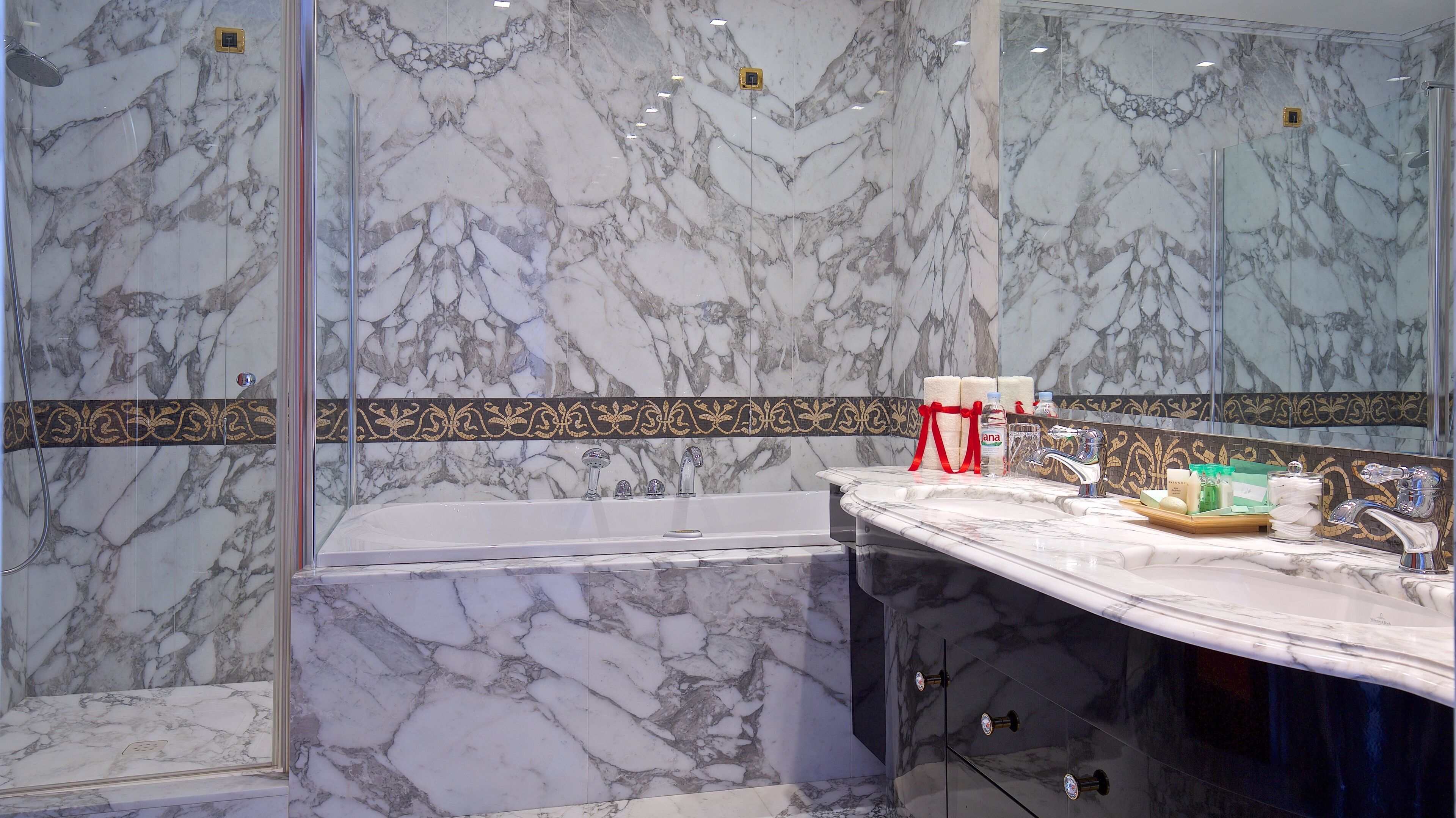 Un bagno con parete in marmo, vasca, mobile toilette con specchio e articoli da toilette.