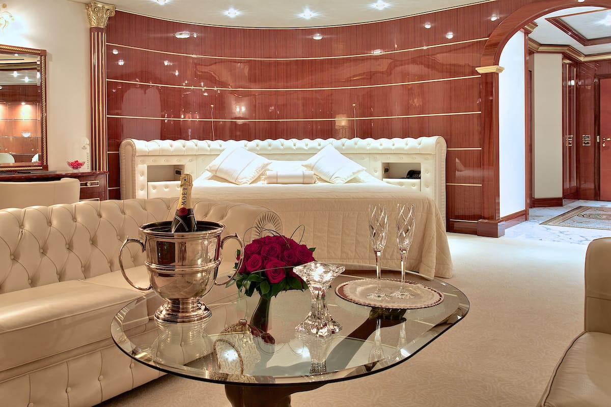 A luxurious bedroom with a large bed, a sitting area with a glass table, and a mirror above a desk.