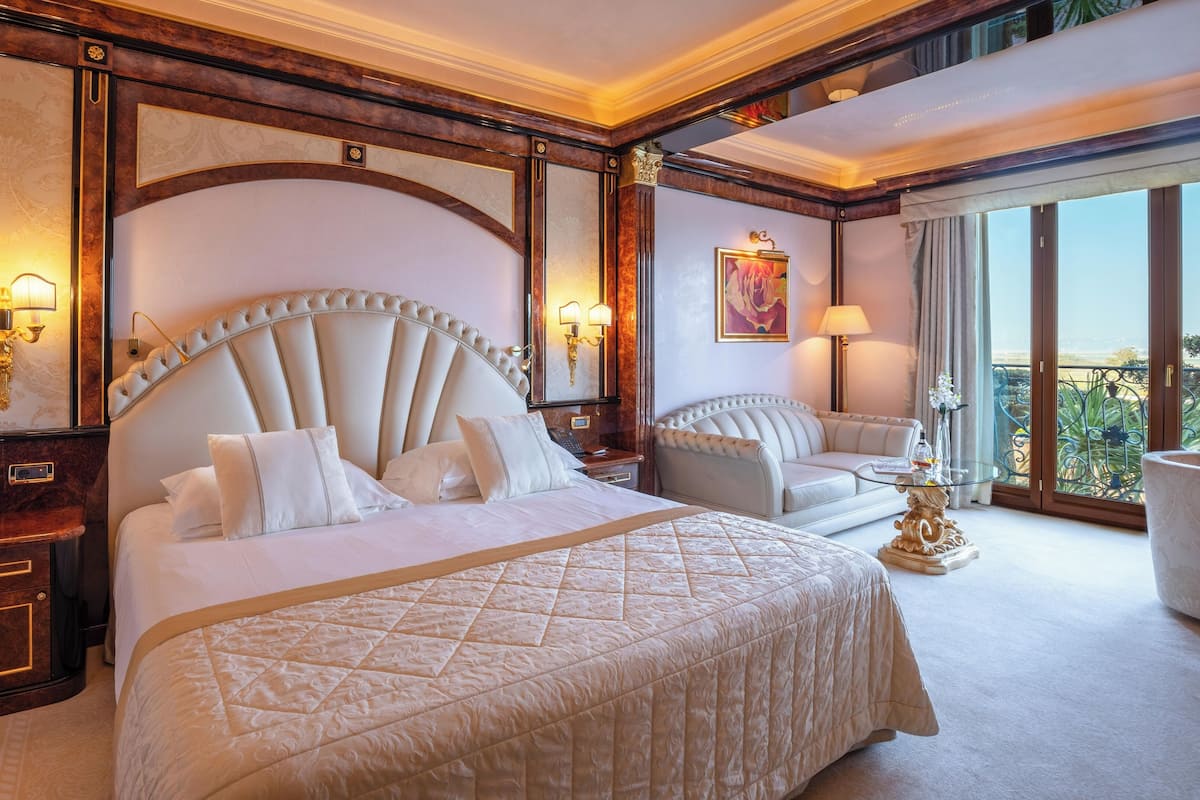 A luxurious hotel room with a large bed, a sofa, and a balcony with a view.