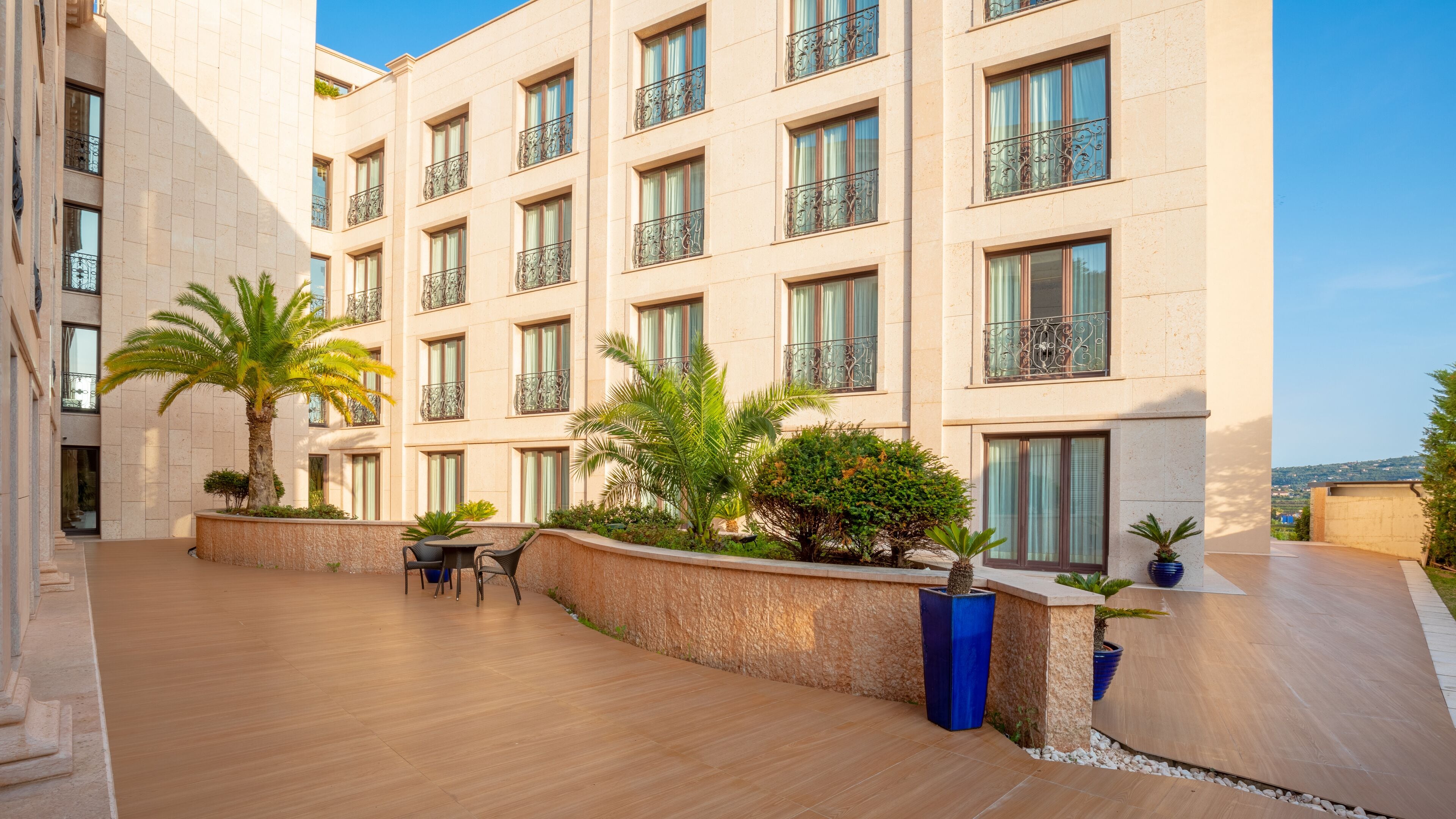 A modern hotel with a courtyard featuring palm trees, a seating area, and a view of the surrounding landscape.