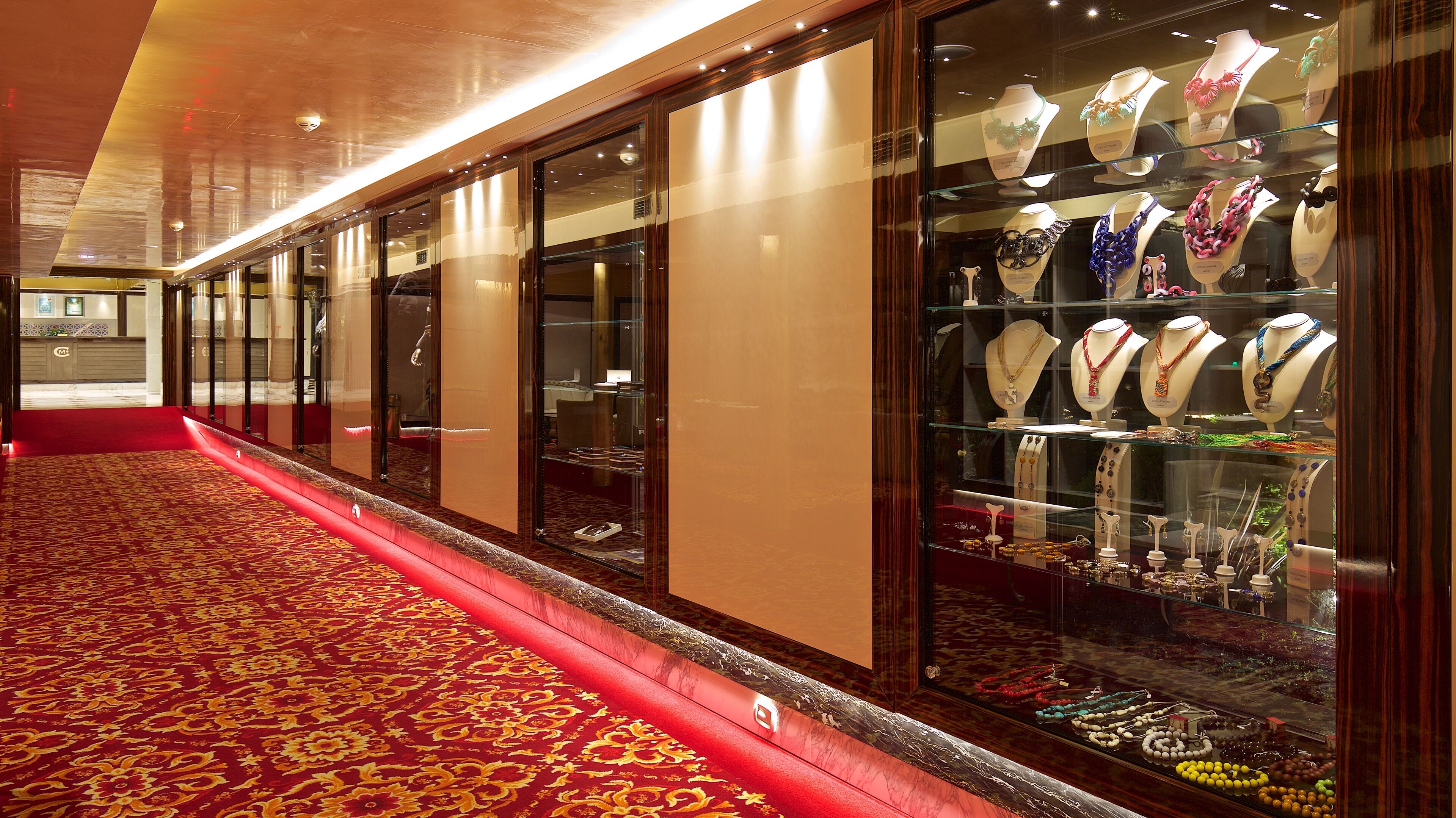 A corridor with a red carpet leading to a glass display case filled with jewelry.