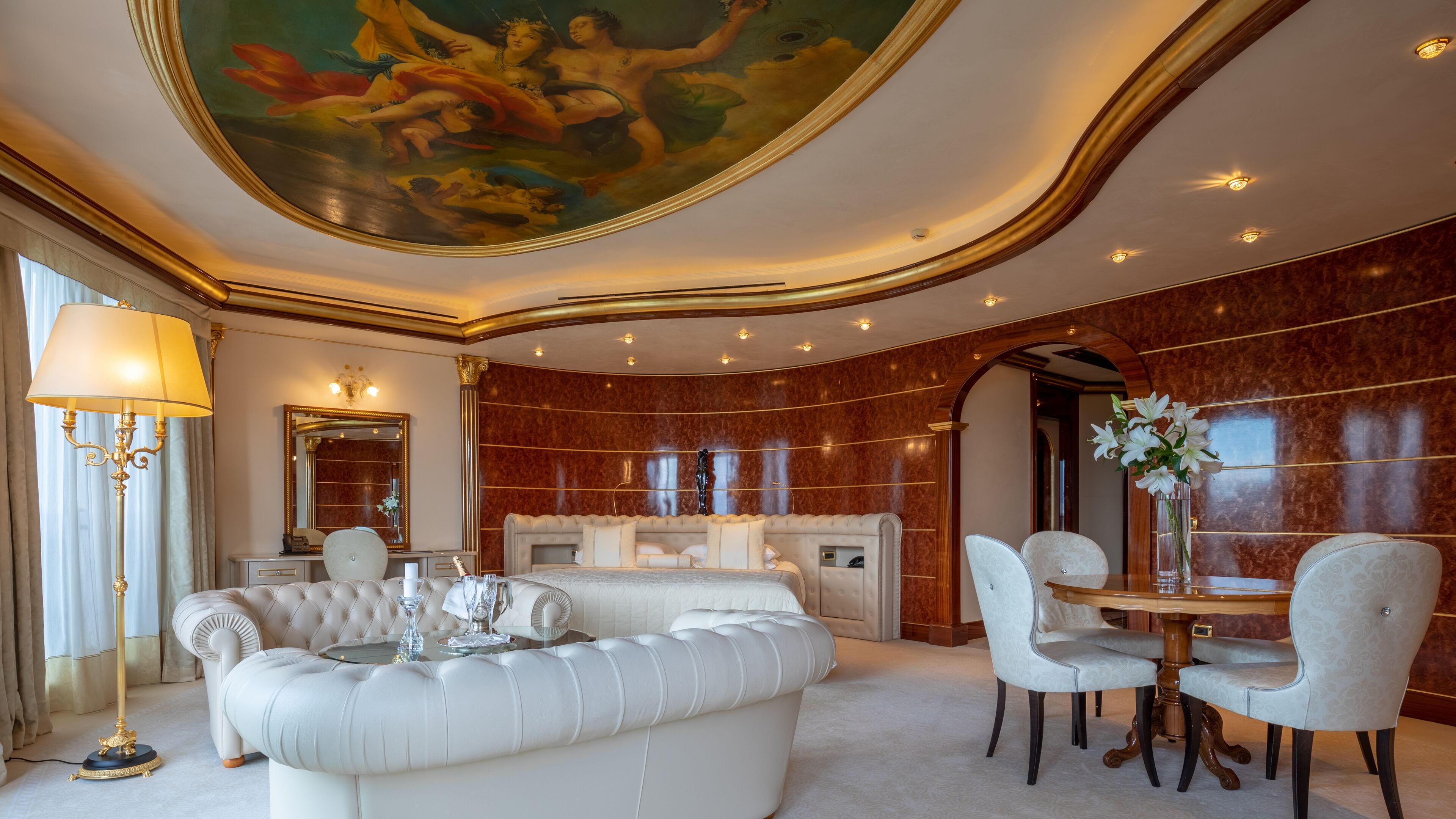 A luxurious room with a large white tufted sofa, a dining table with chairs, a chandelier, and a large mirror.