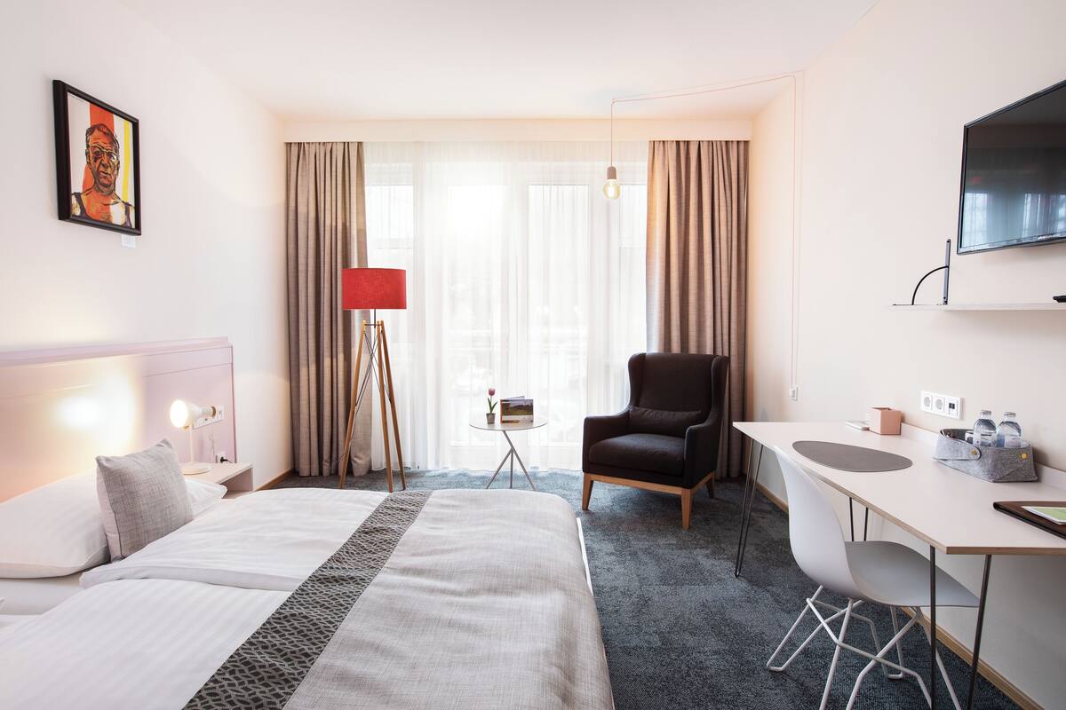 A hotel room with a bed, desk, chair, TV, and curtains.
