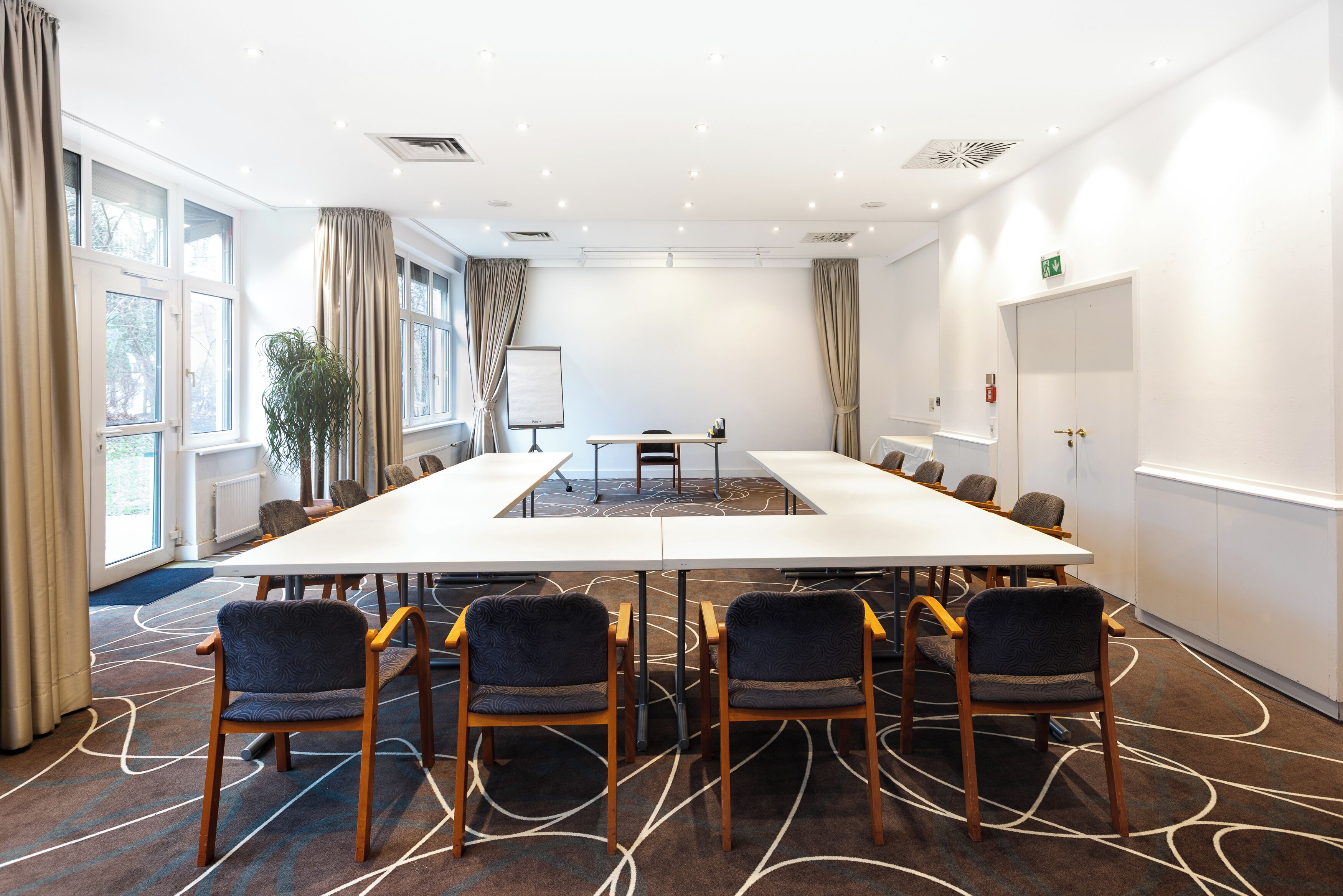 A conference room with a long table, chairs, a whiteboard, and a plant.
