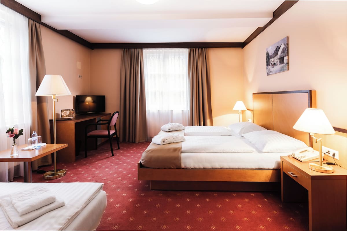 A hotel room with a bed, bedside table, lamp, desk, chair, TV, and curtains.