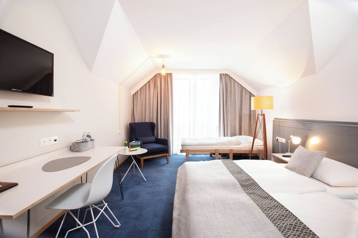 A hotel room with a bed, desk, chair, TV, and a lamp.