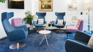 A modern lounge area with blue and pink chairs, a round table, and a painting on the wall. - Höldrichsmühle (Hinterbruhl)