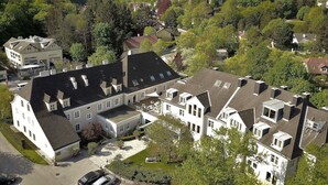 A large, multi-story building with multiple roof levels and dormer windows, surrounded by lush greenery and hills. - Höldrichsmühle (Hinterbruhl)