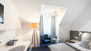 A modern hotel room with a bed, a desk, a chair, a small table, and a TV. - Höldrichsmühle (Hinterbruhl)