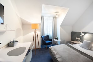 A modern hotel room with a bed, a desk, a chair, a small table, and a TV. - Höldrichsmühle (Hinterbruhl)