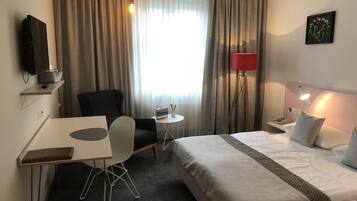 Ein Hotelzimmer mit einem Bett, einem Schreibtisch, einem Stuhl, einem kleinen Tisch, einer Lampe und einem Bild an der Wand.